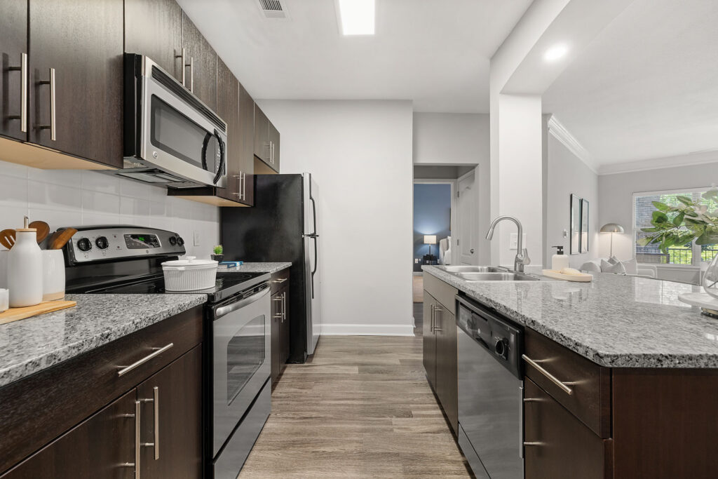 Modern kitchen with dark cabinets, stainless steel appliances, granite countertops, a double sink, and wood-style flooring; open layout with a view into the living area.
